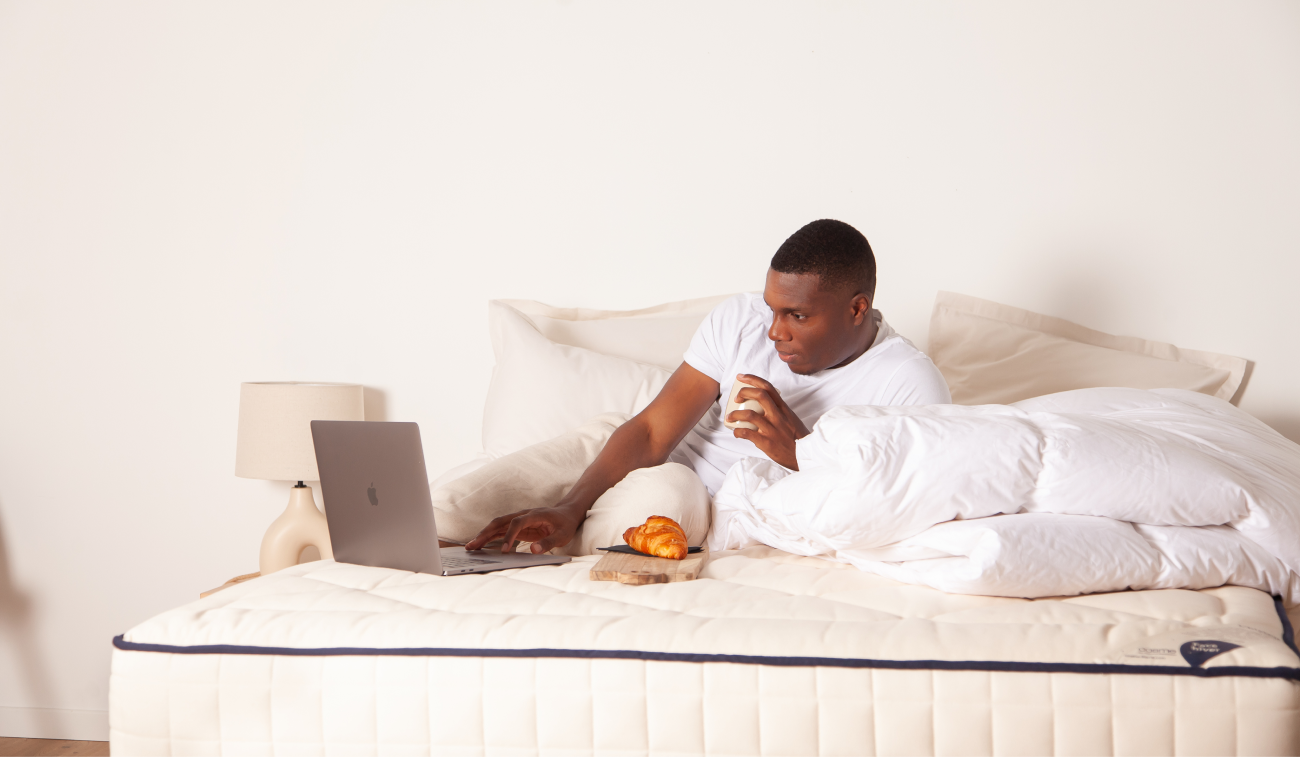 Homme allongé sur son lit prenant le petit-déjeuner devant son ordinateur