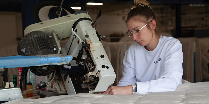 Coralie galonnant un matelas Cosme, dernière étape de la fabrication du matelas Cosme